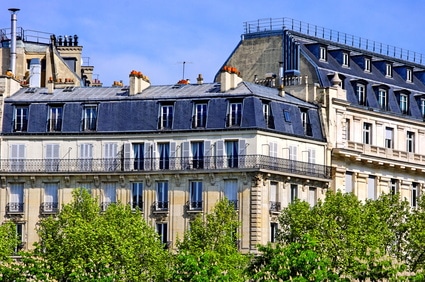 Immeubles de pierre blanche aux toits gris avec arbres.